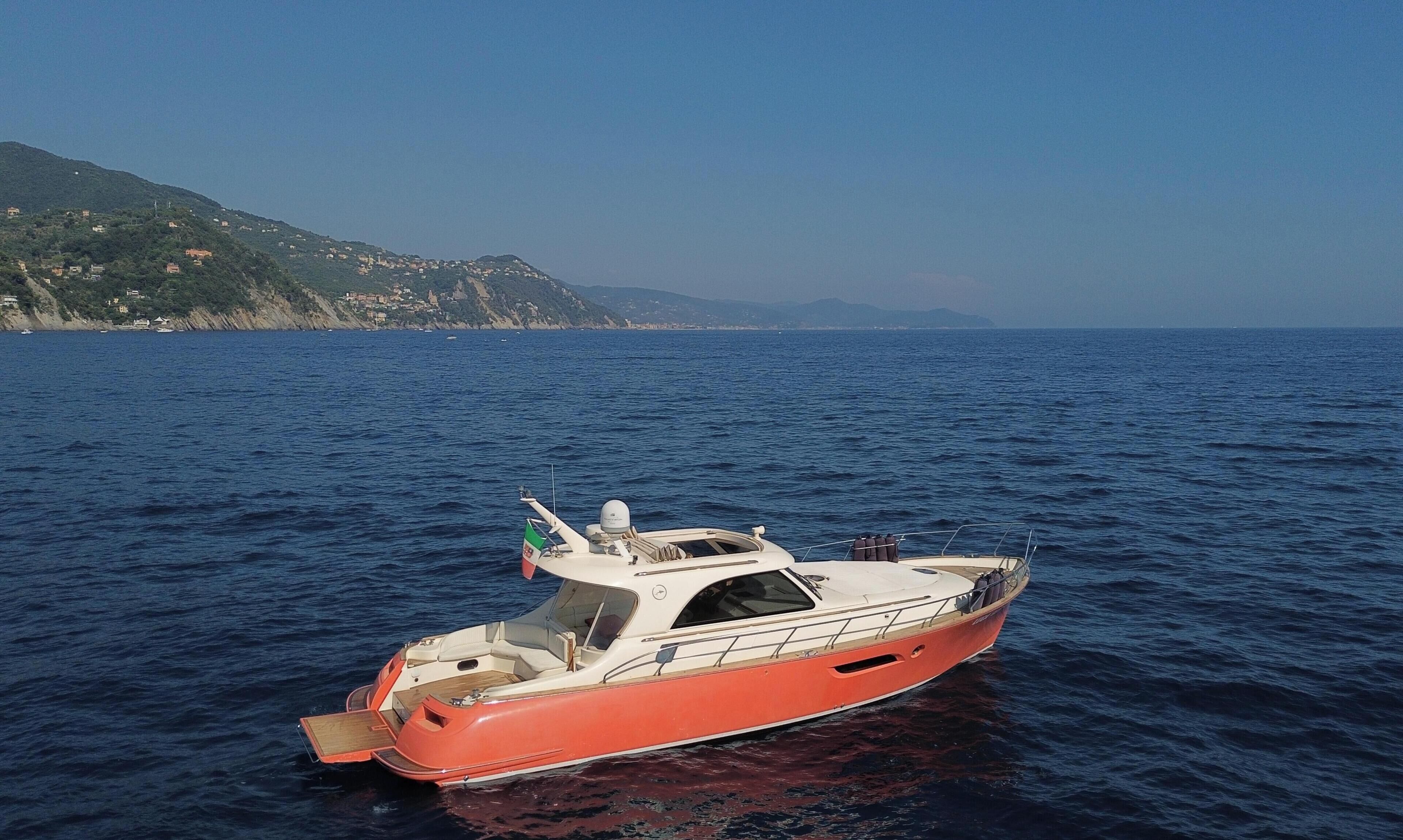 A small, red boat on calm water with a clear view of a coastline and hills in the background.