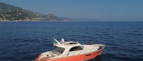 Um pequeno barco vermelho em águas calmas, com vista clara para a costa e colinas ao fundo.