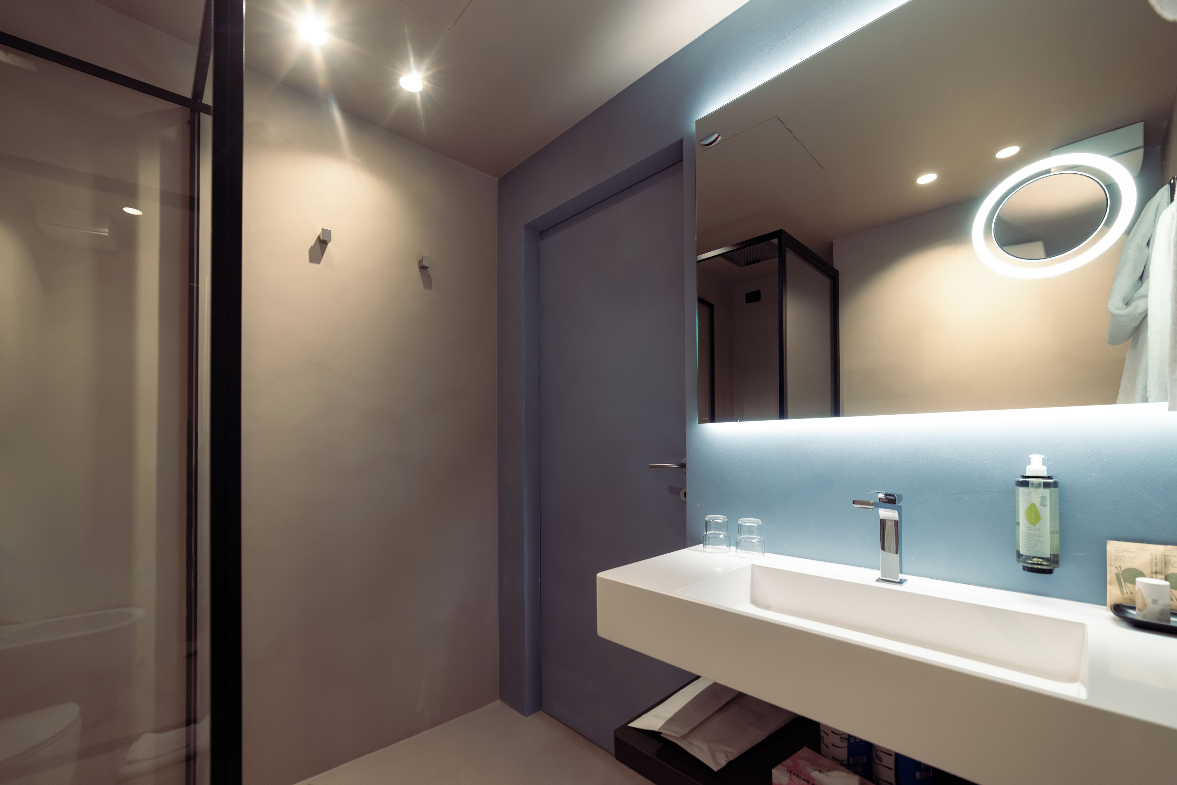 Un baño moderno con un lavamanos blanco, un espejo de marco redondo y una zona de ducha.