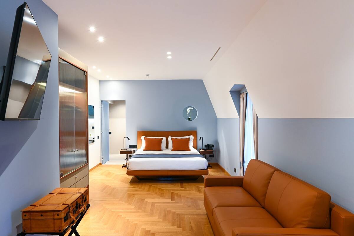 Una habitación de hotel moderna con una cama, un sofá, piso de madera y un espejo grande.