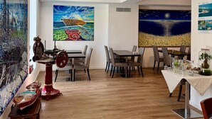 Un comedor con suelo de madera, una mesa con sillas y dos cuadros grandes en las paredes.