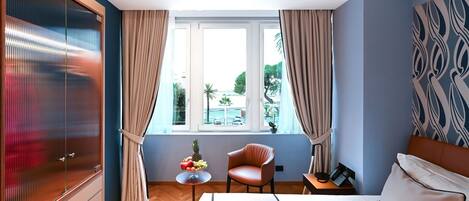Habitación de hotel con cama, una silla, una mesita con fruta, un teléfono en una mesita auxiliar y una ventana con cortinas.