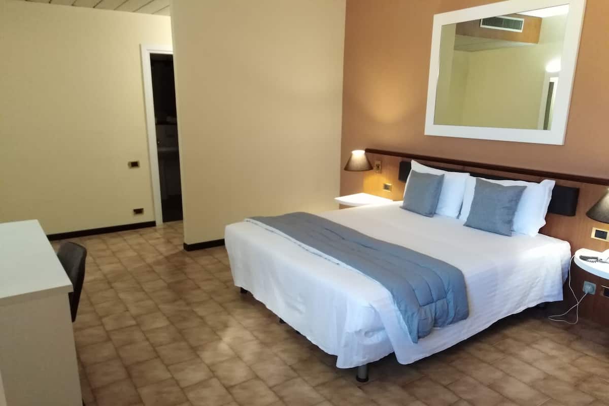 Une chambre d’hôtel avec un lit, une table de chevet, une lampe et un miroir au mur.