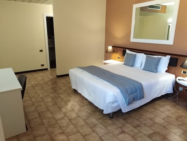 Una habitación de hotel con cama, mesita de noche, lámpara y espejo en la pared.