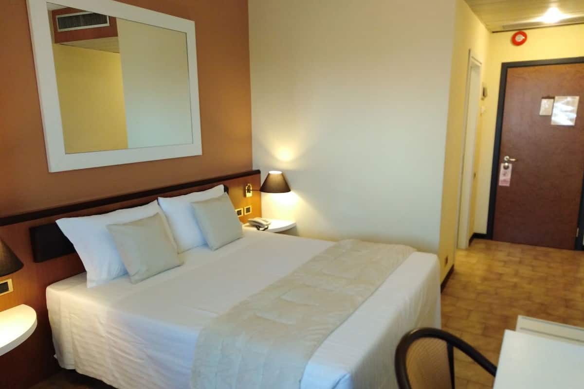 Une chambre d’hôtel avec un lit, une lampe de chevet et une porte avec une pancarte.