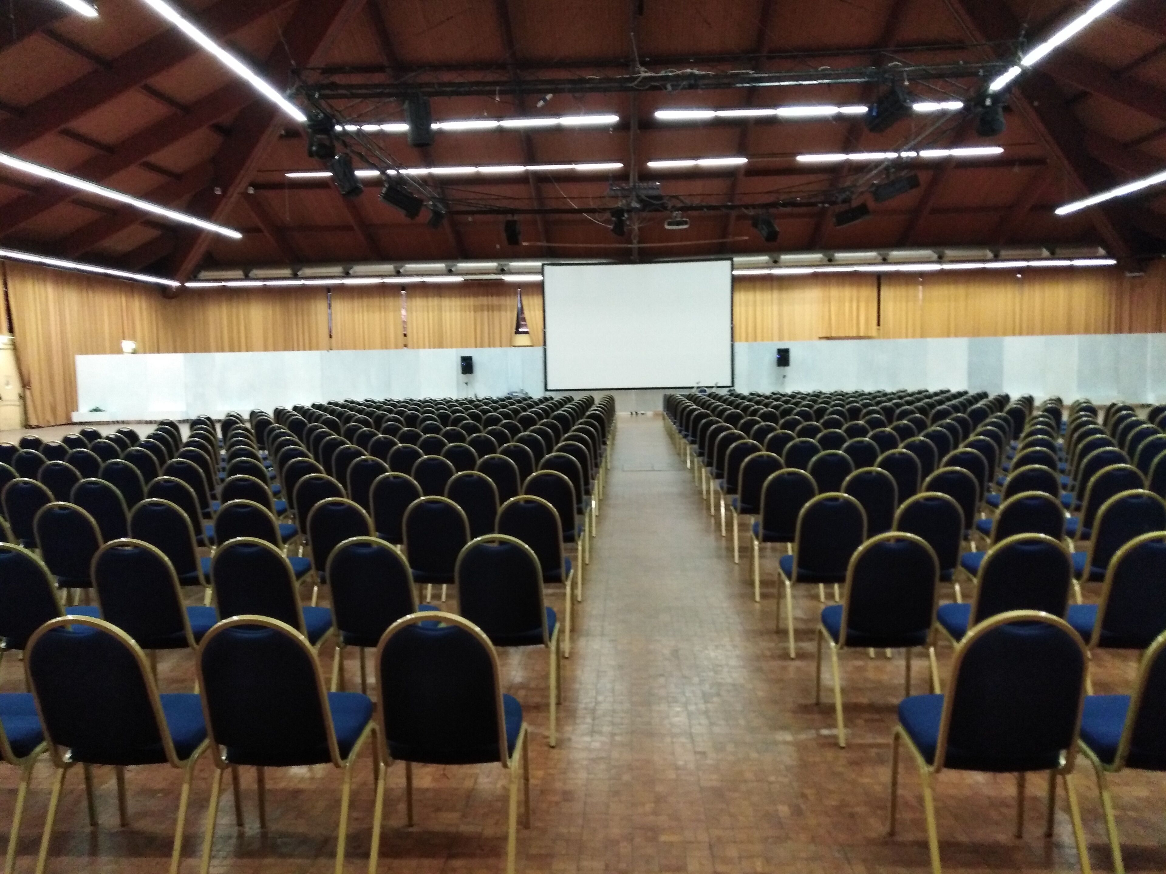 Un grand auditorium intérieur, avec des rangées de chaises bleues et une scène à l’avant.