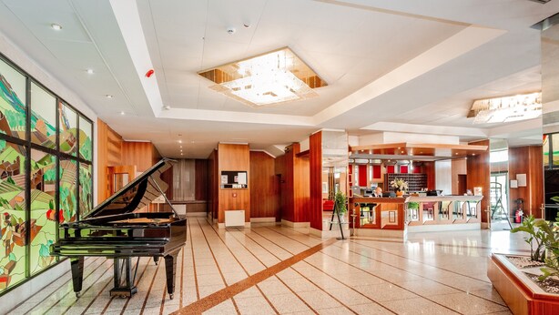 Un pianoforte a coda in un'ampia hall con pavimento piastrellato, elementi in legno e un'area reception moderna.