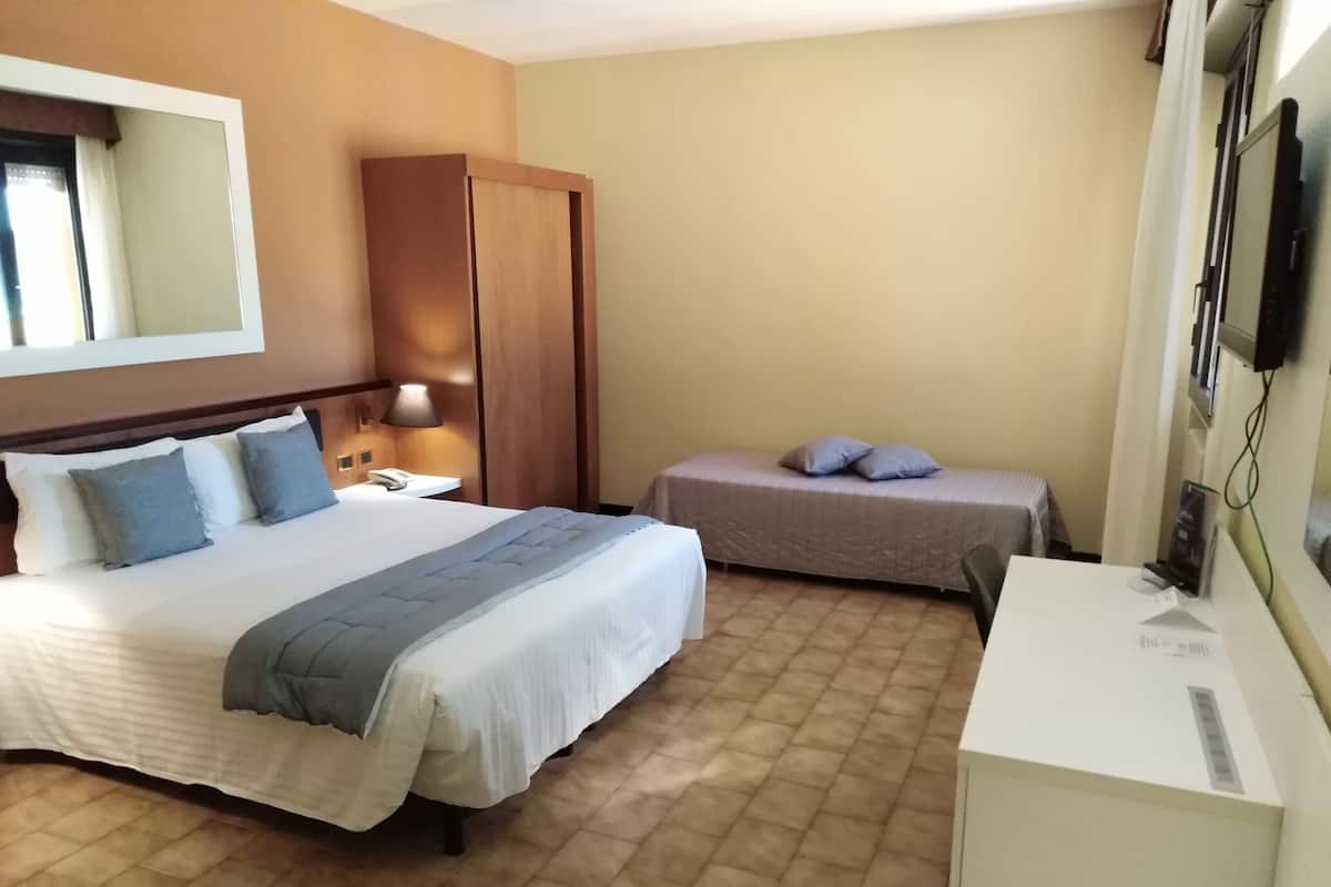 Une chambre d’hôtel avec un grand lit, un lit plus petit, un bureau, une armoire et un téléviseur.