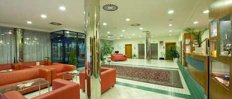 A hotel lobby with red sofas, a large pillar, a reception desk, and a carpeted area.