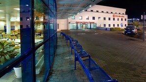 Een hotel nabij het vliegveld, met een glazen gevel, een overdekt terras en een verharde entree.