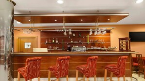 Een bar met houten toogbladen, rode bekleden barkrukken en hangende verlichtingsarmaturen.