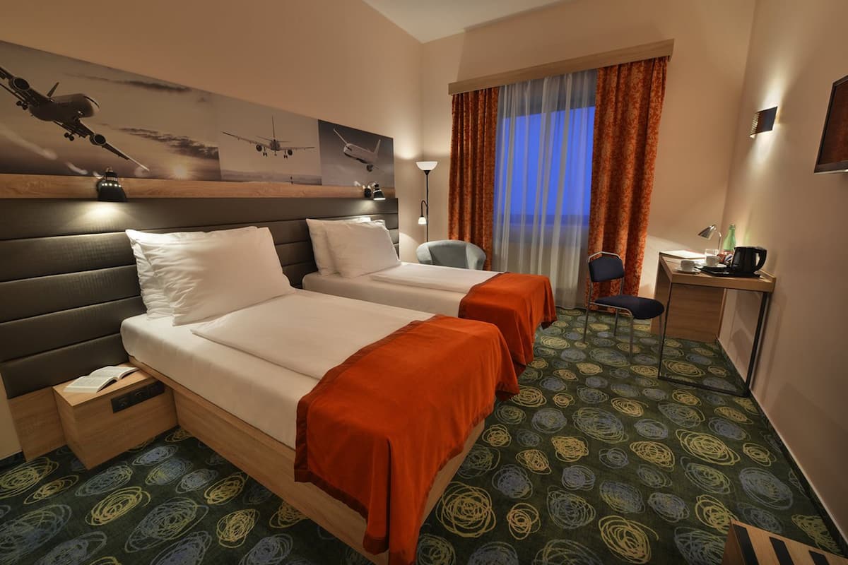 A hotel room with two beds, a desk, a chair, and a large window with curtains.