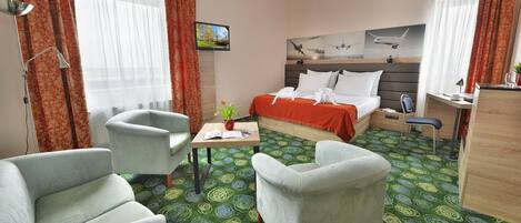 Habitación de hotel con cama, dos sillones, escritorio, televisor y ventana con cortinas.