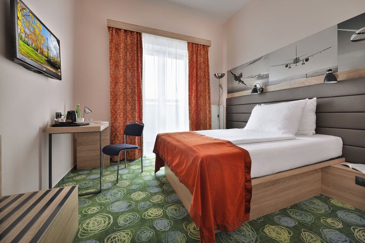 A hotel room with a bed, a desk, a chair, and a window with curtains.