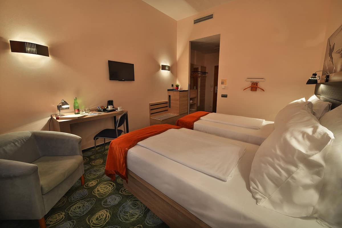 A hotel room with two beds, a desk, a chair, a TV, and a coat rack.