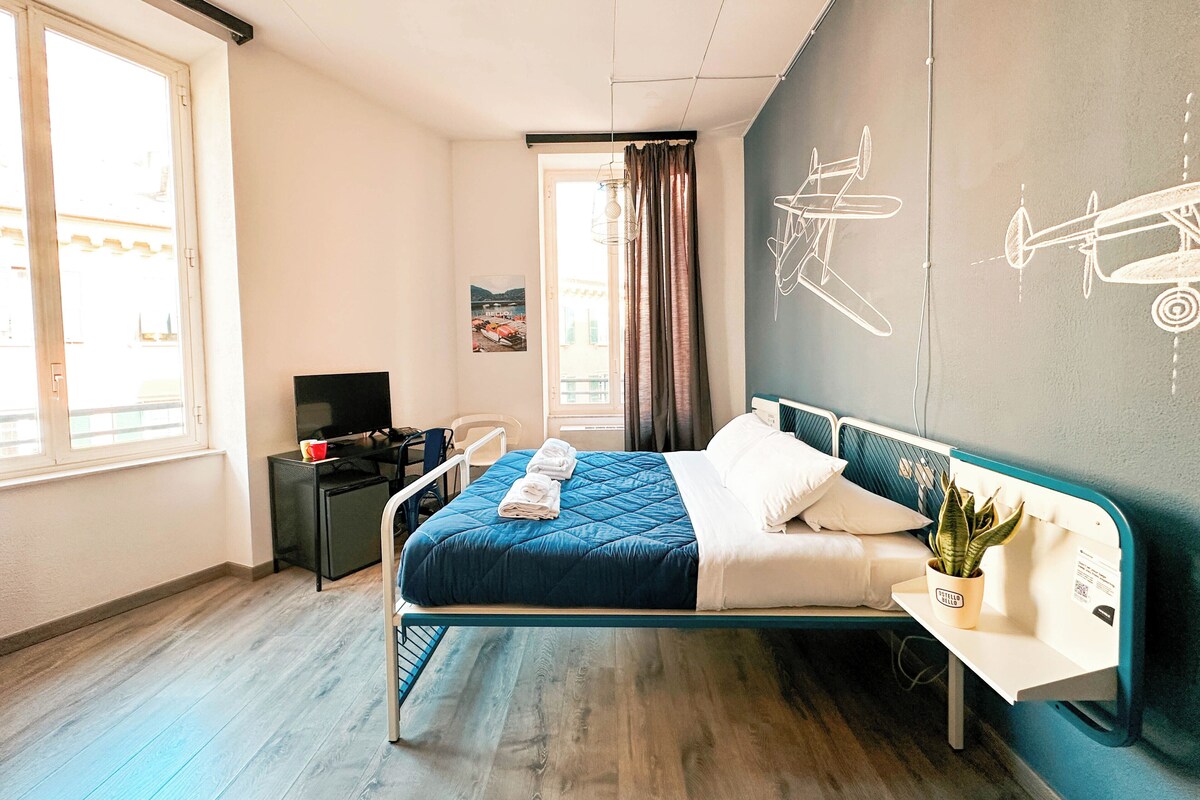 A hotel room with a bed, a desk, a chair, a TV, and a window.