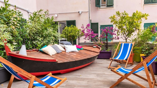 A wooden boat-shaped seating area with cushions, surrounded by potted plants and blue-striped chairs.