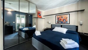 A hotel room with two beds, a large mirror, a painting, and a desk with a chair.