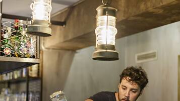 Un barman prépare un cocktail dans un bar décoré de guirlandes lumineuses et doté d’étagères remplies de bouteilles.
