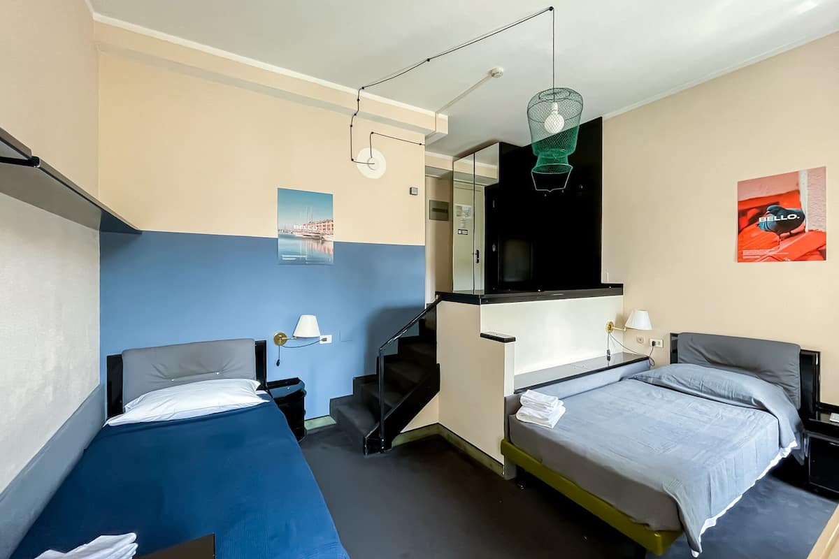 Hotellihuone, jossa on kaksi erillistä sänkyä, pieni työpöytä, tuoli, televisio ja portaat, jotka johtavat ylempään kerrokseen.