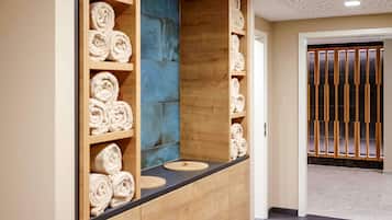 Bathroom features a vanity with a countertop and cabinet, a shelf unit with towels, and a tiled floor.