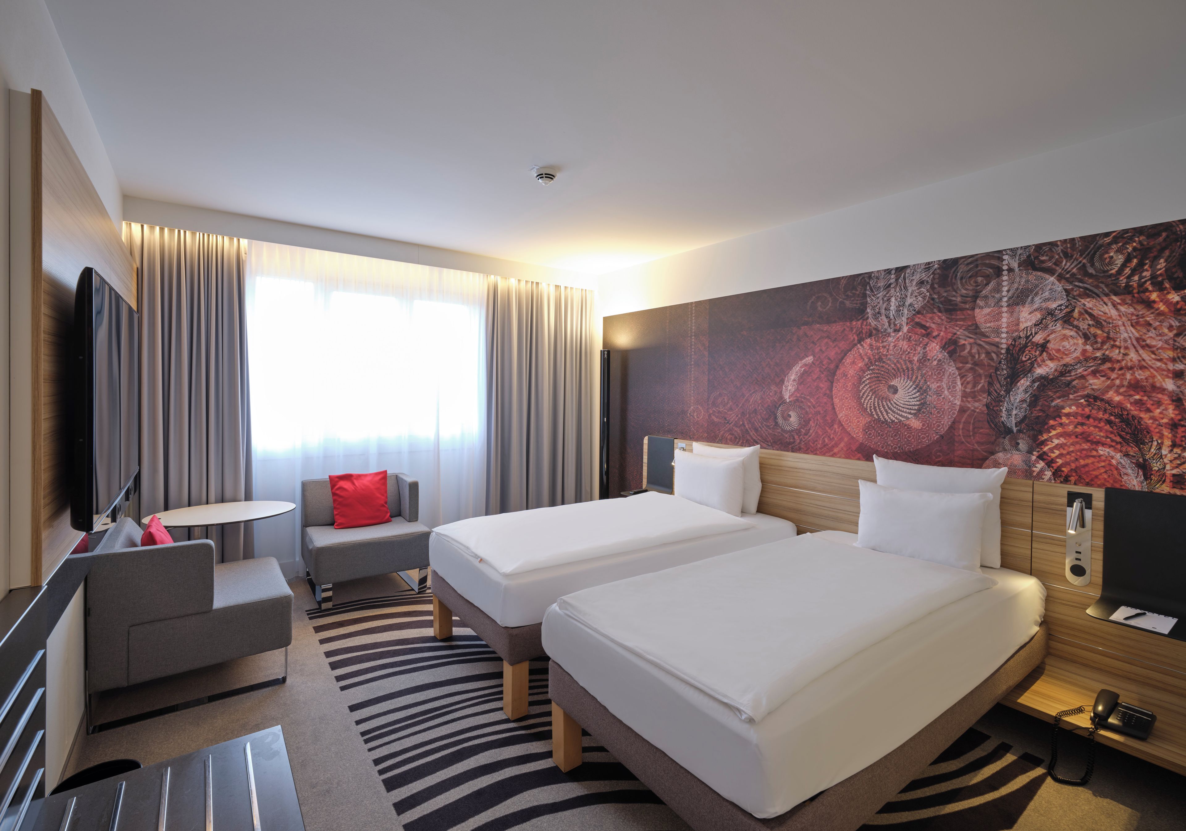 A hotel room with two beds, a sofa, a TV, and a large abstract painting on the wall.