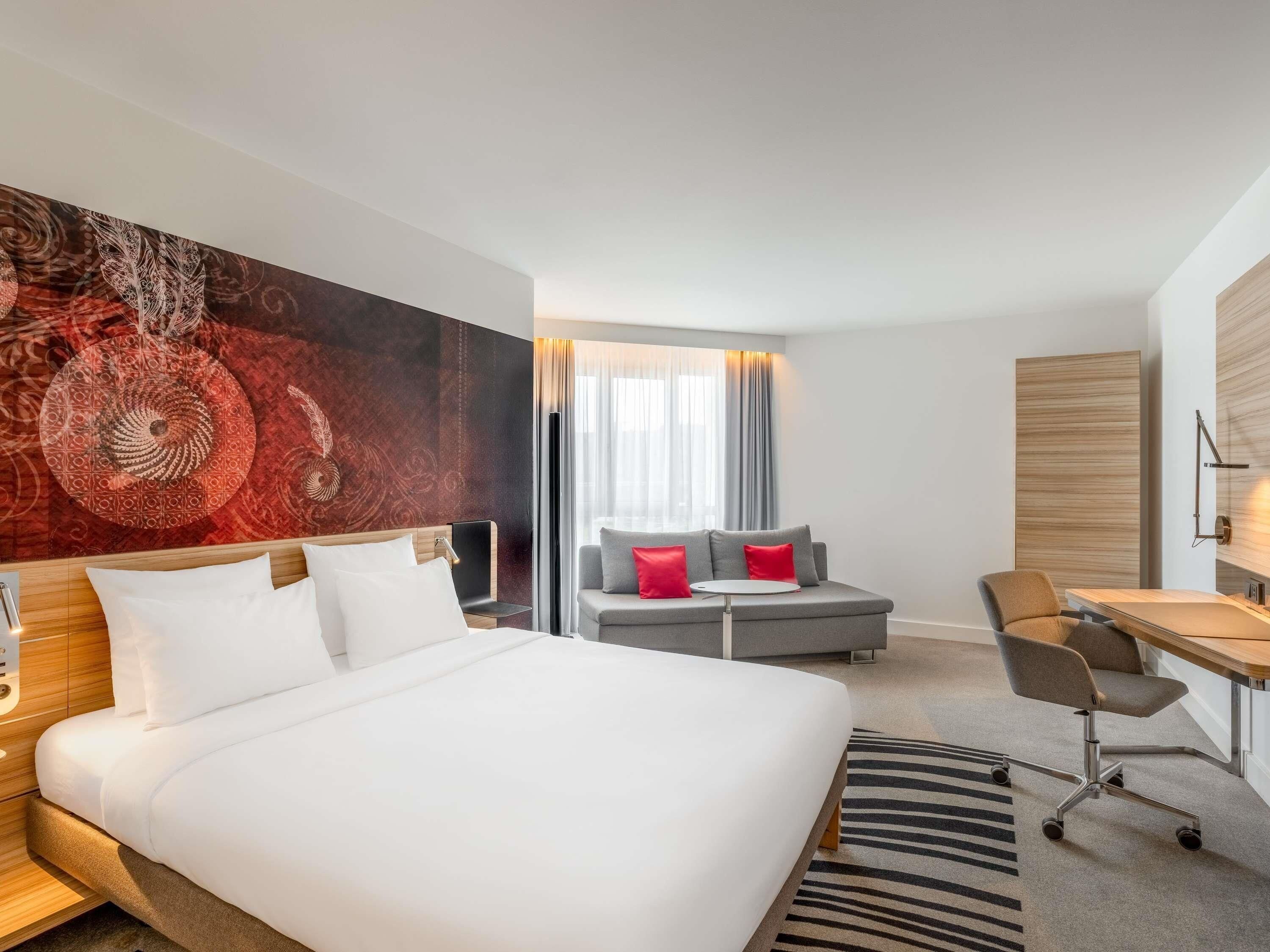 Una habitación de hotel con una cama grande, un sofá gris, un escritorio y una gran obra de arte abstracto en la pared.