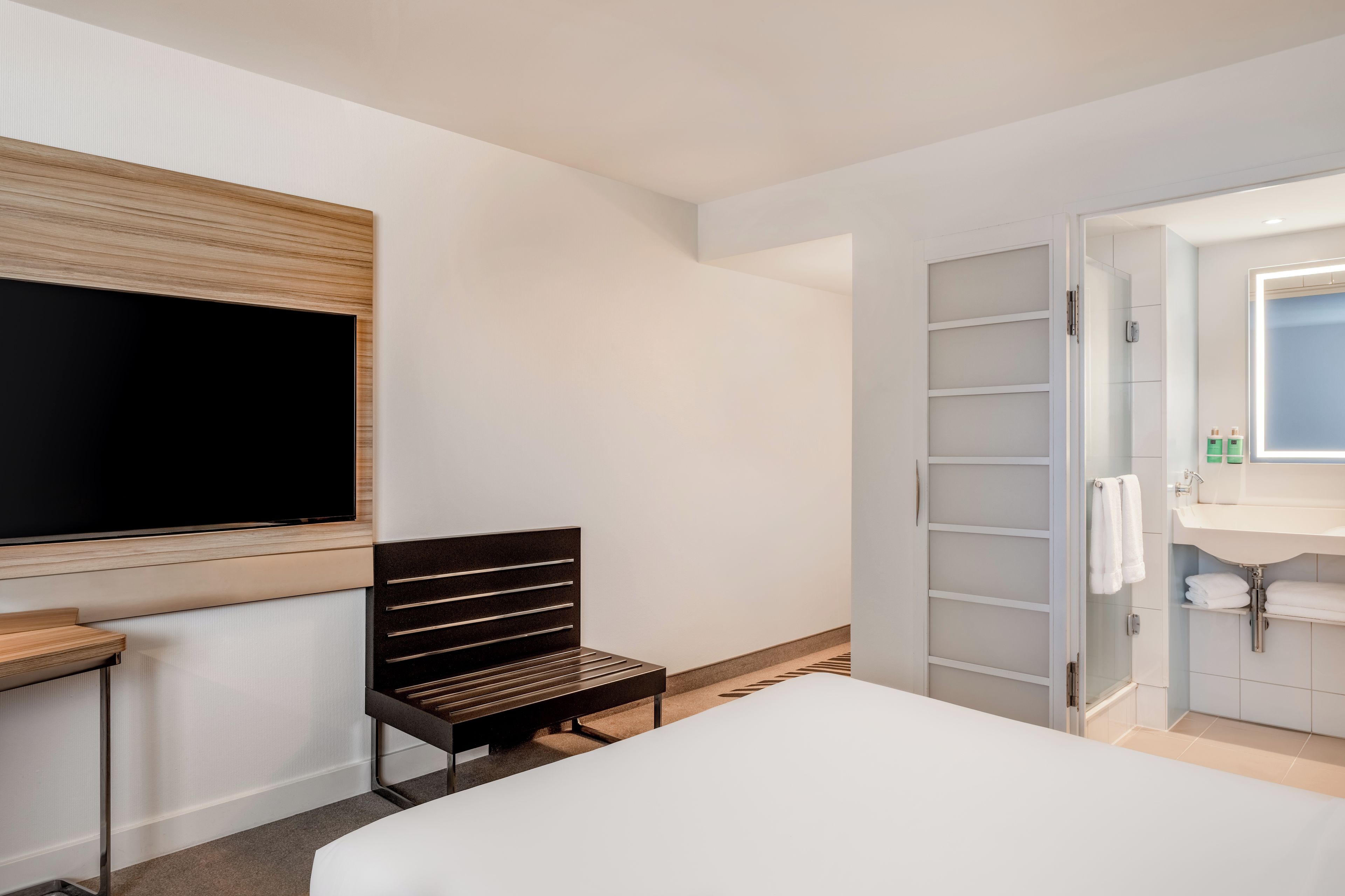 Une chambre d’hôtel équipée d’un lit, d’une télévision, d’un bureau, d’une chaise, d’une armoire et d’une salle de bain.