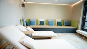 A modern spa room with two lounge chairs, a bench with cushions, and a wooden floor. - Novotel Muenchen City (Munich)