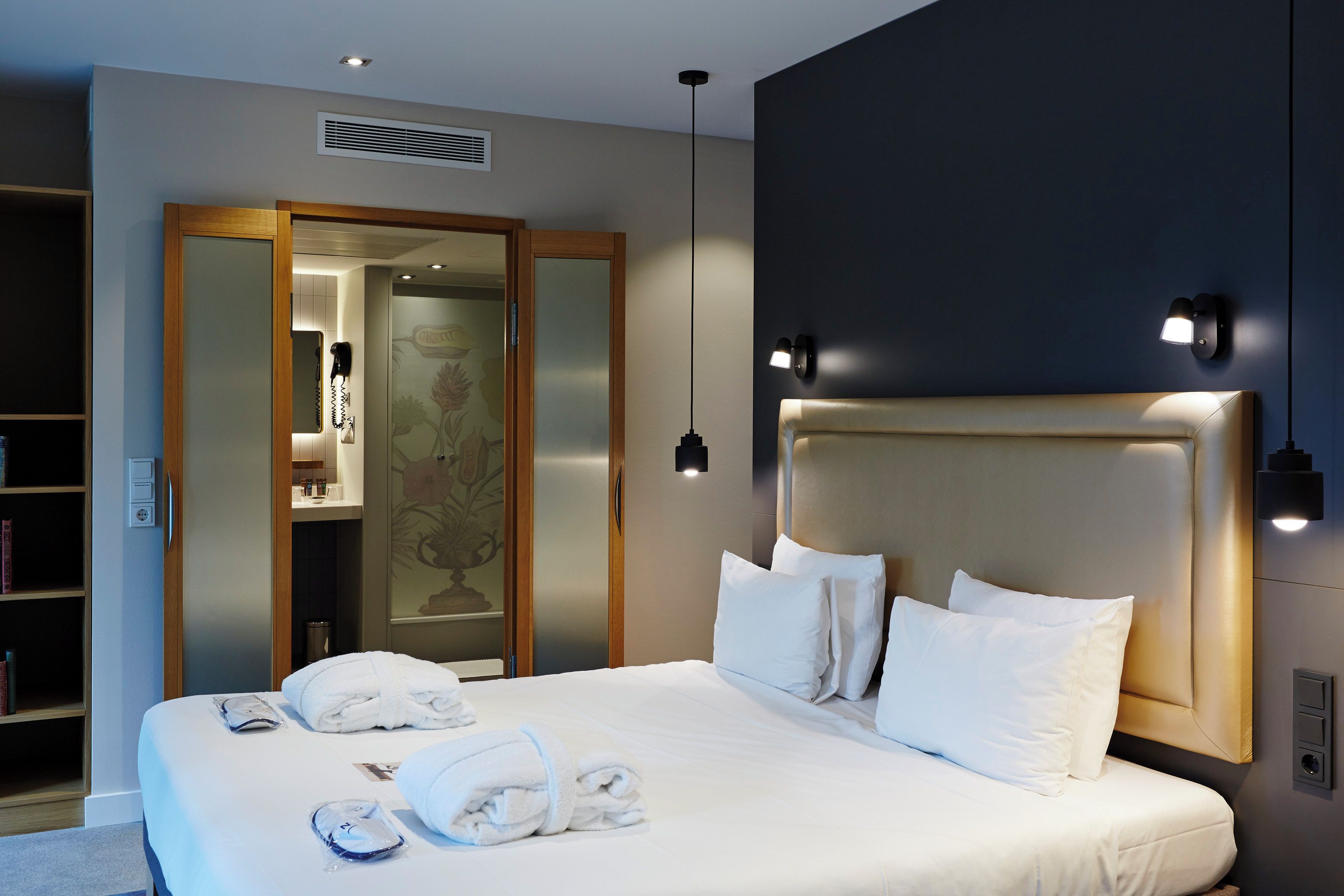 Une chambre d’hôtel avec un grand lit, une armoire, un miroir et un luminaire fixé au mur.