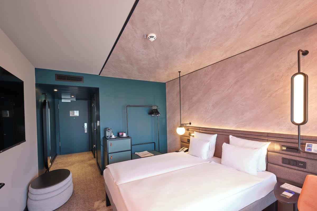 Ein modernes Hotelzimmer mit einem großen Bett, einem Schreibtisch, einem Sessel, einer Lampe und einer Minibar.