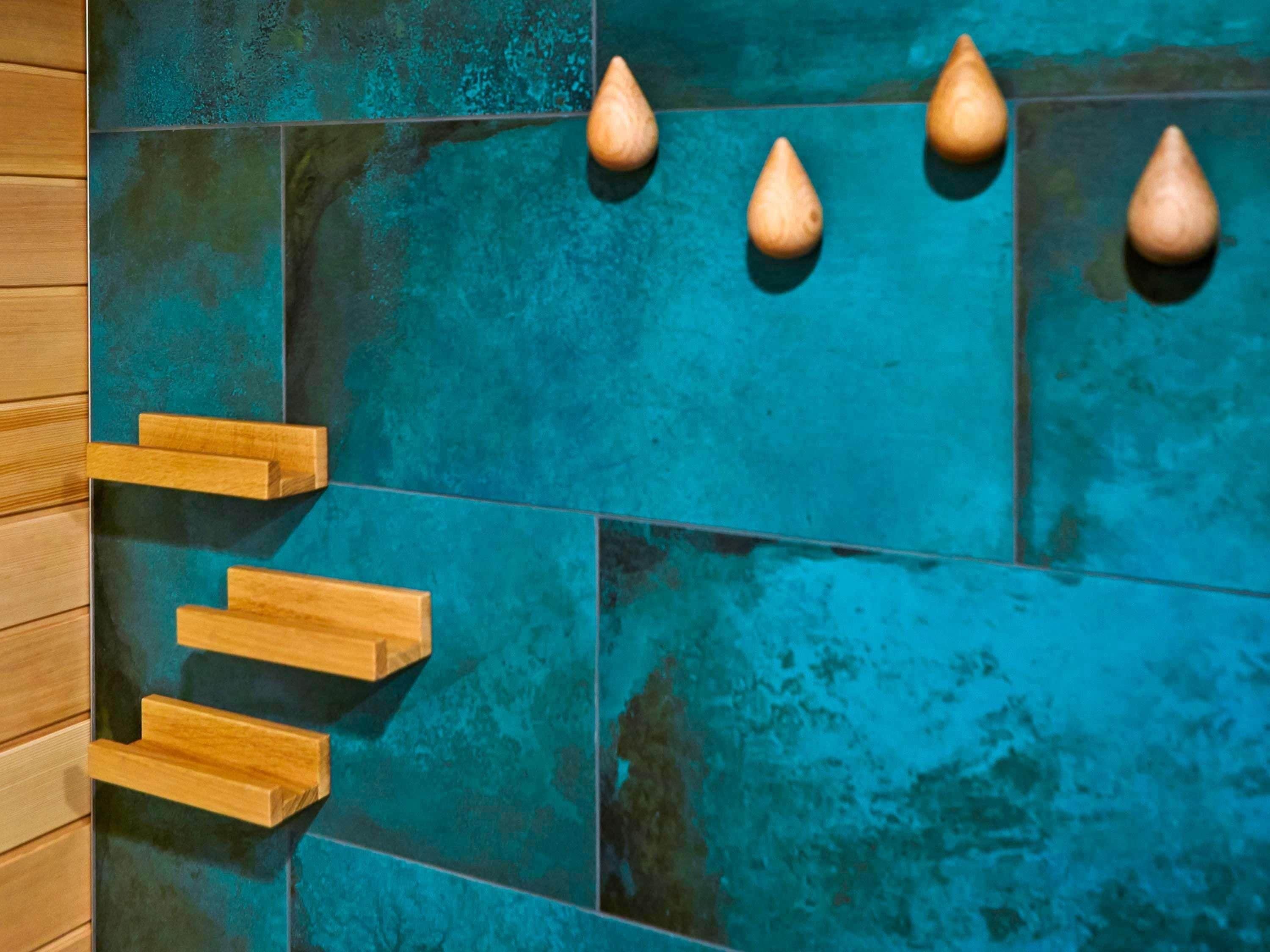 A bathroom with teal tiles and wooden towel racks.