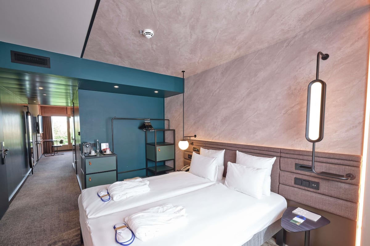 Ein Hotelzimmer mit Bett, Nachttischen, einem Schreibtisch, einem Spiegel und Blick auf den Flur.