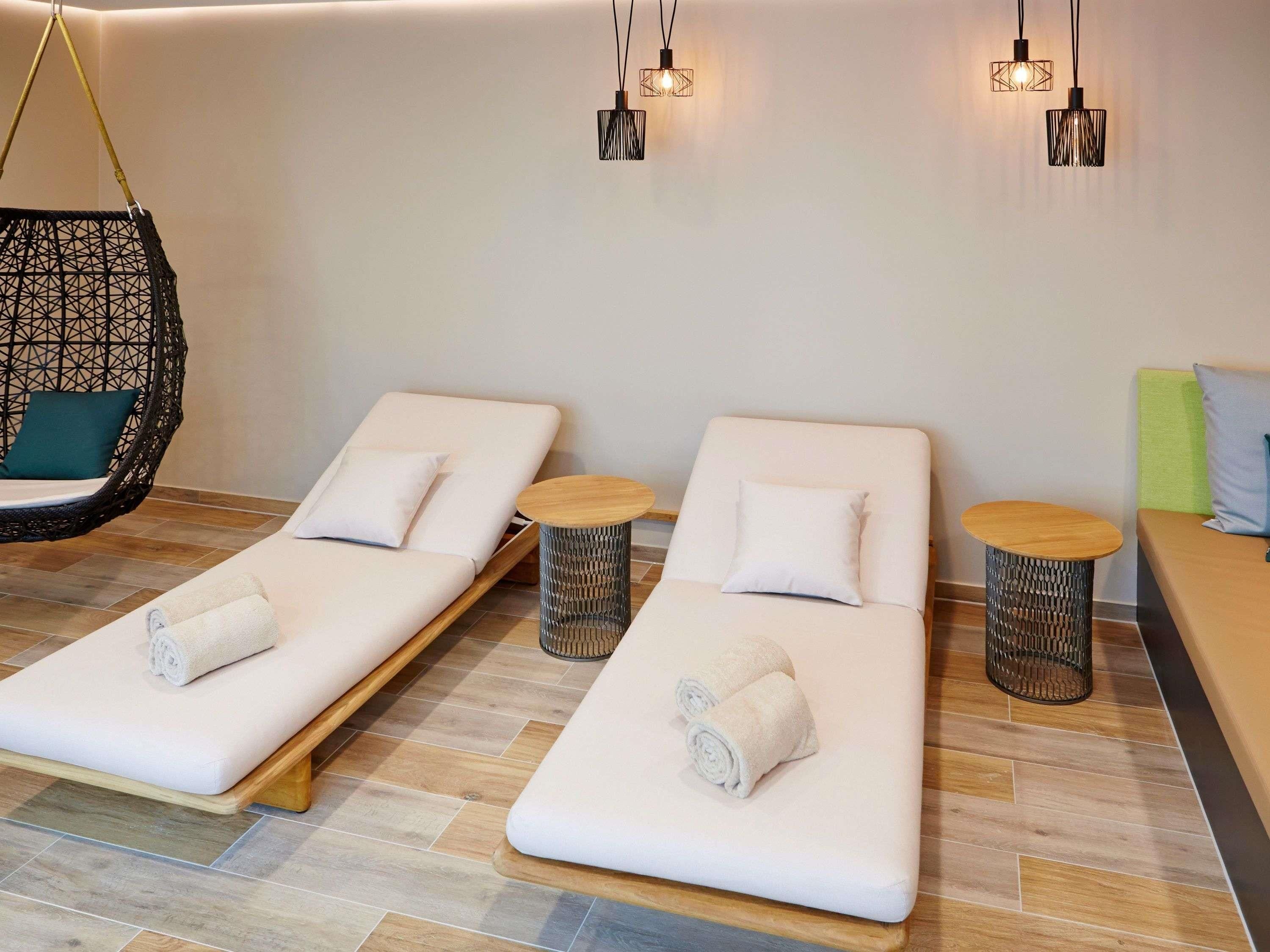 A spa room with two massage tables, a hanging chair, and two small round tables with towels.