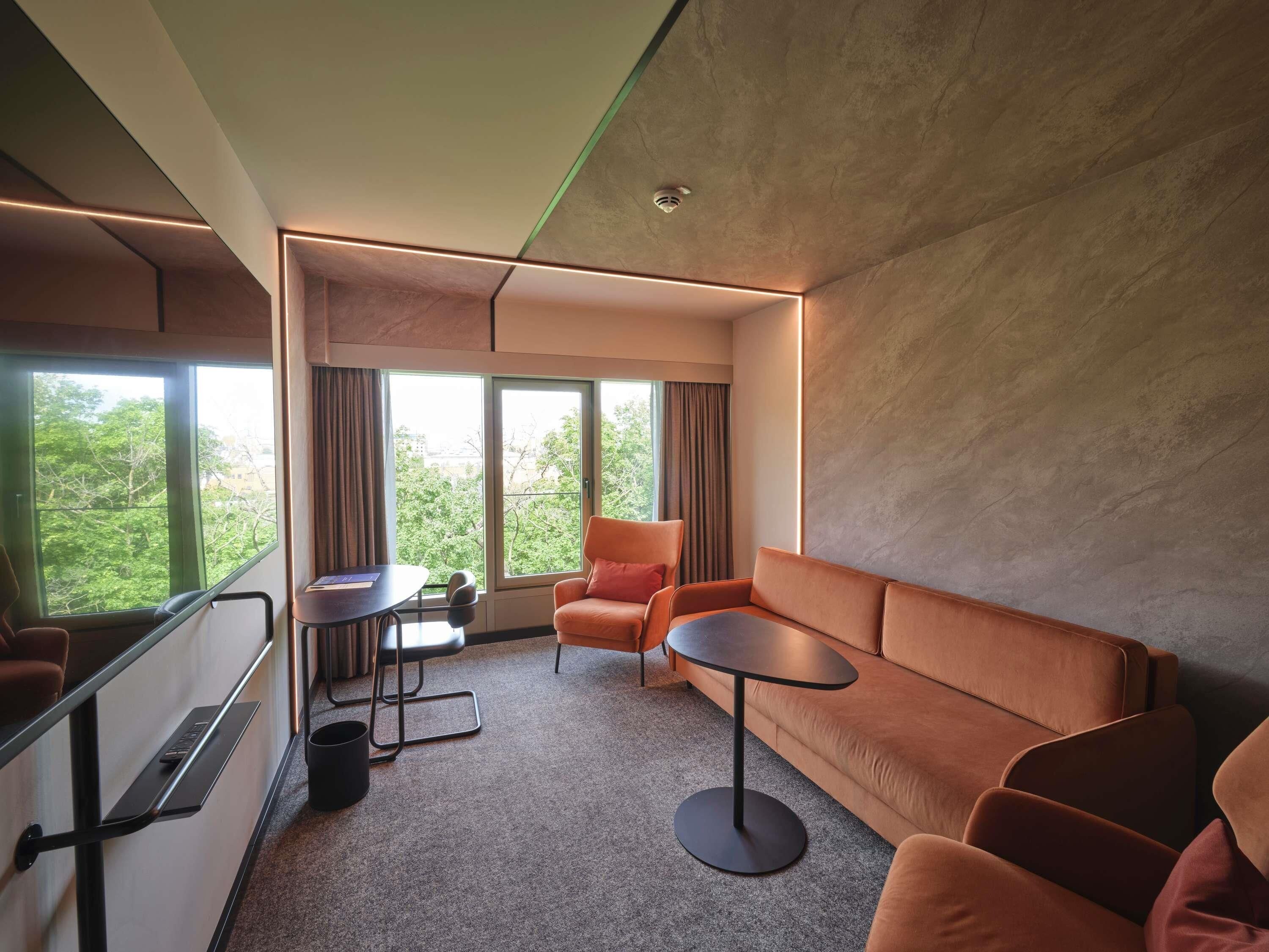 Een moderne hotelkamer met een groot raam, een bank, een klein tafeltje en een stoel.