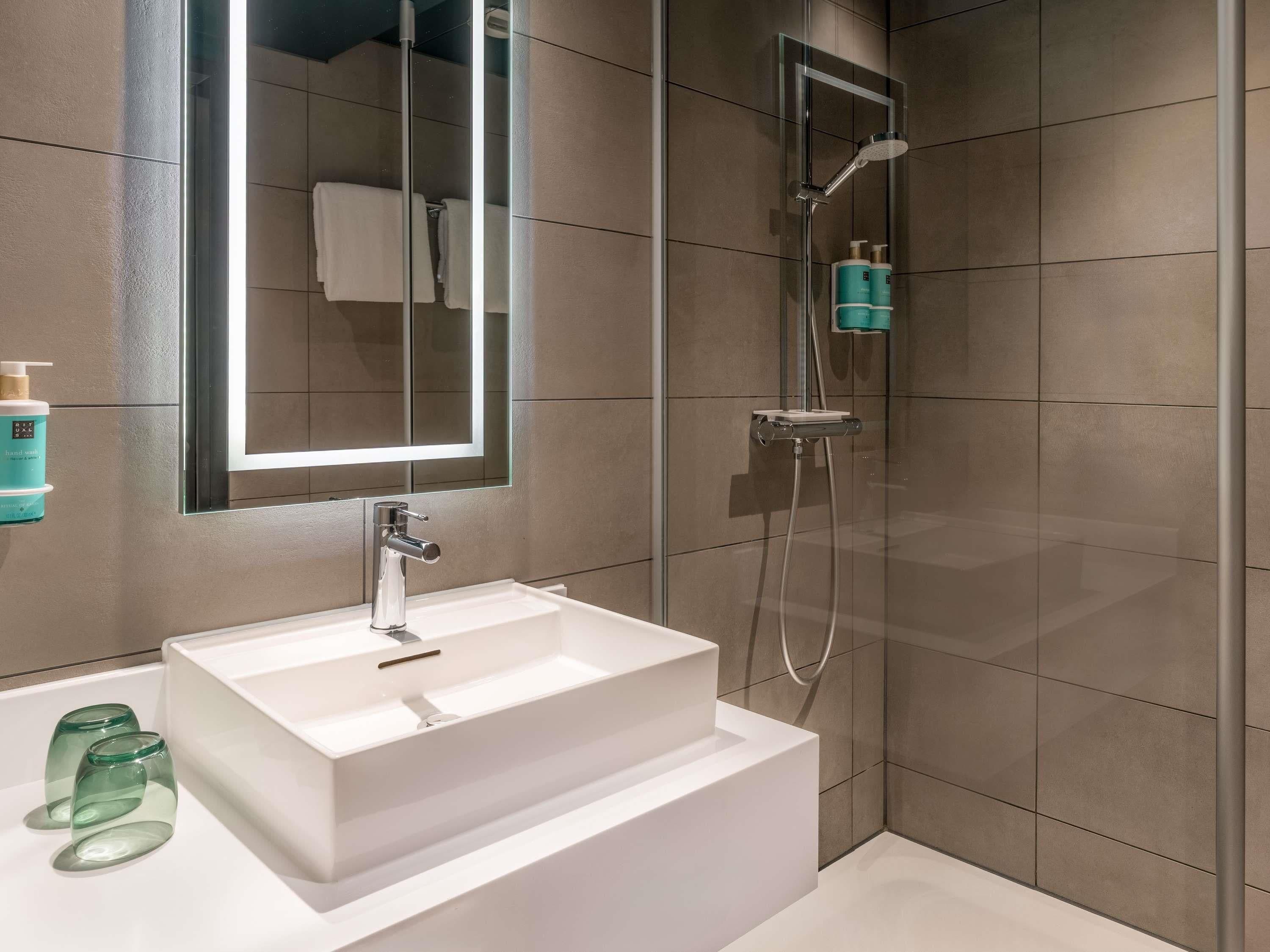 Un baño moderno con un lavamanos blanco, cabina de ducha de vidrio y un espejo grande.