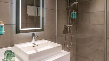 Un baño moderno con un lavamanos blanco, cabina de ducha de vidrio y un espejo grande.