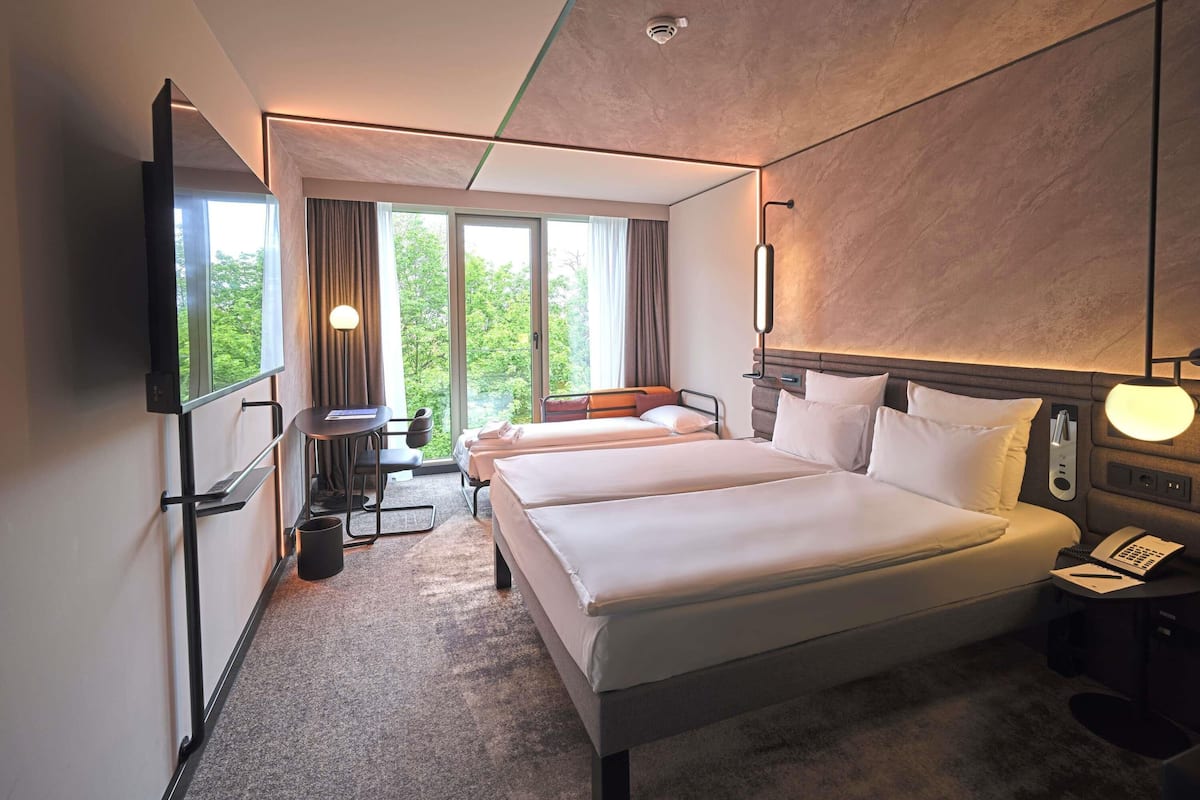 Ein Hotelzimmer mit einem großen Bett, einem Schreibtisch mit Stuhl, einem Fernseher und einem Fenster mit Vorhängen.