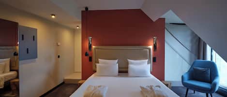 A hotel room with a large bed, two bedside tables, a blue armchair, and a view of the outdoors.