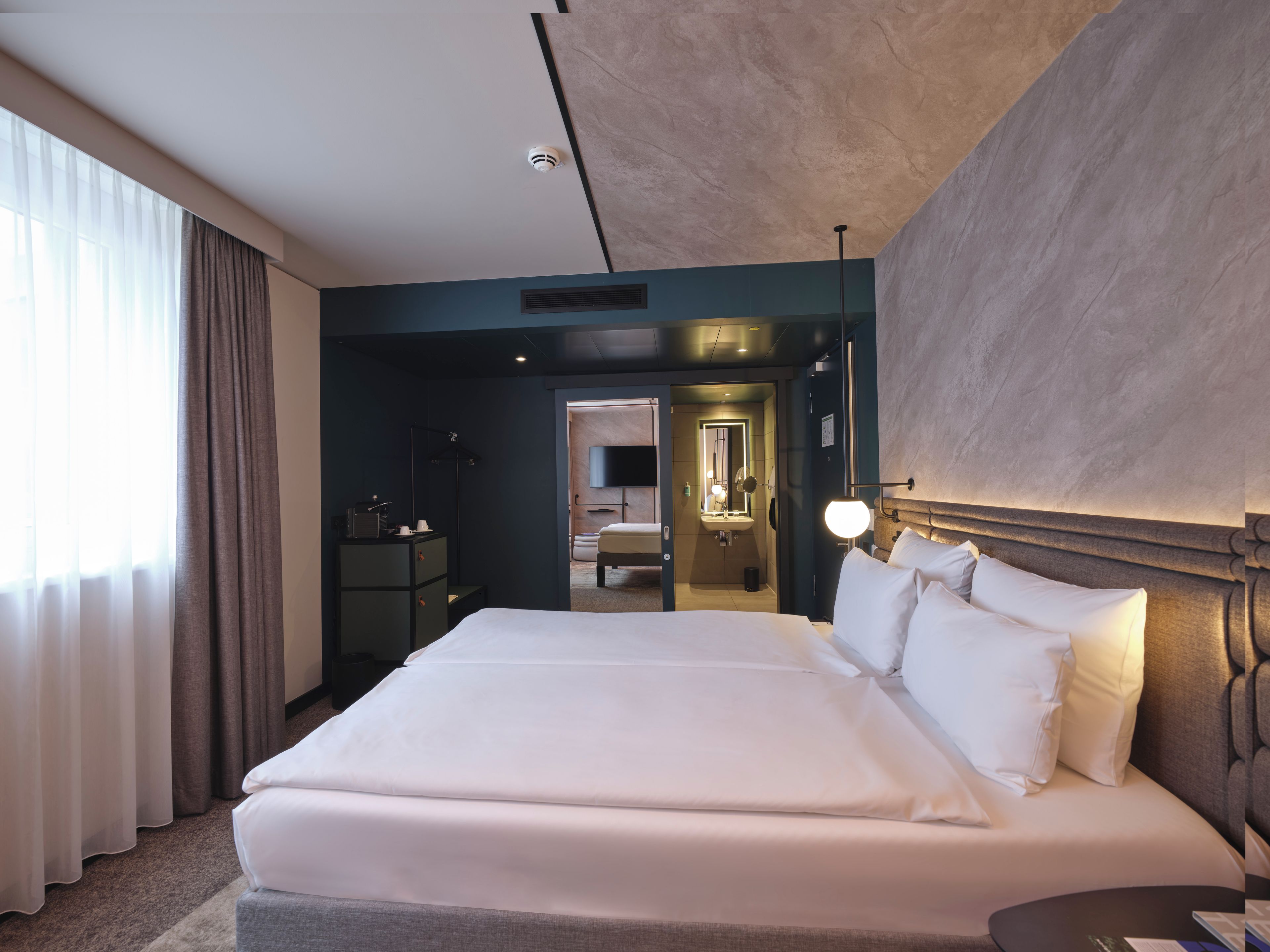 Een hotelkamer met een groot bed, een nachtkastje, een spiegel en uitzicht op de badkamer.