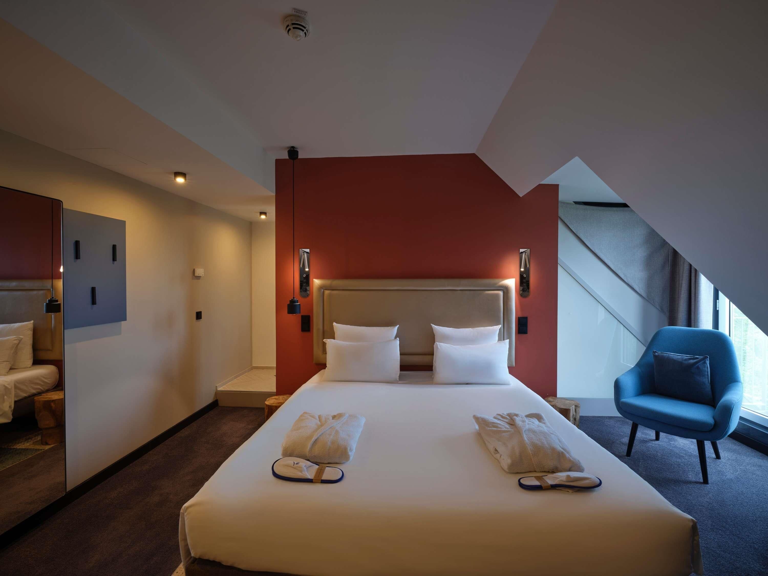 Ein Hotelzimmer mit einem großen Bett, einem blauen Sessel und Blick ins Freie.
