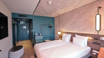 Ein modernes Hotelzimmer mit einem großen Bett, einem Schreibtisch, einem Sessel, einer Lampe und einer Minibar.