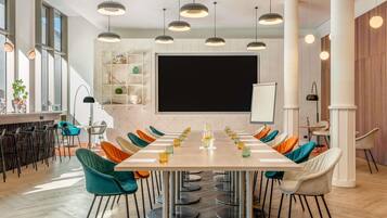 Ein Konferenzraum mit langem Tisch, Stühlen, einer Projektionsleinwand und Pendelleuchten.