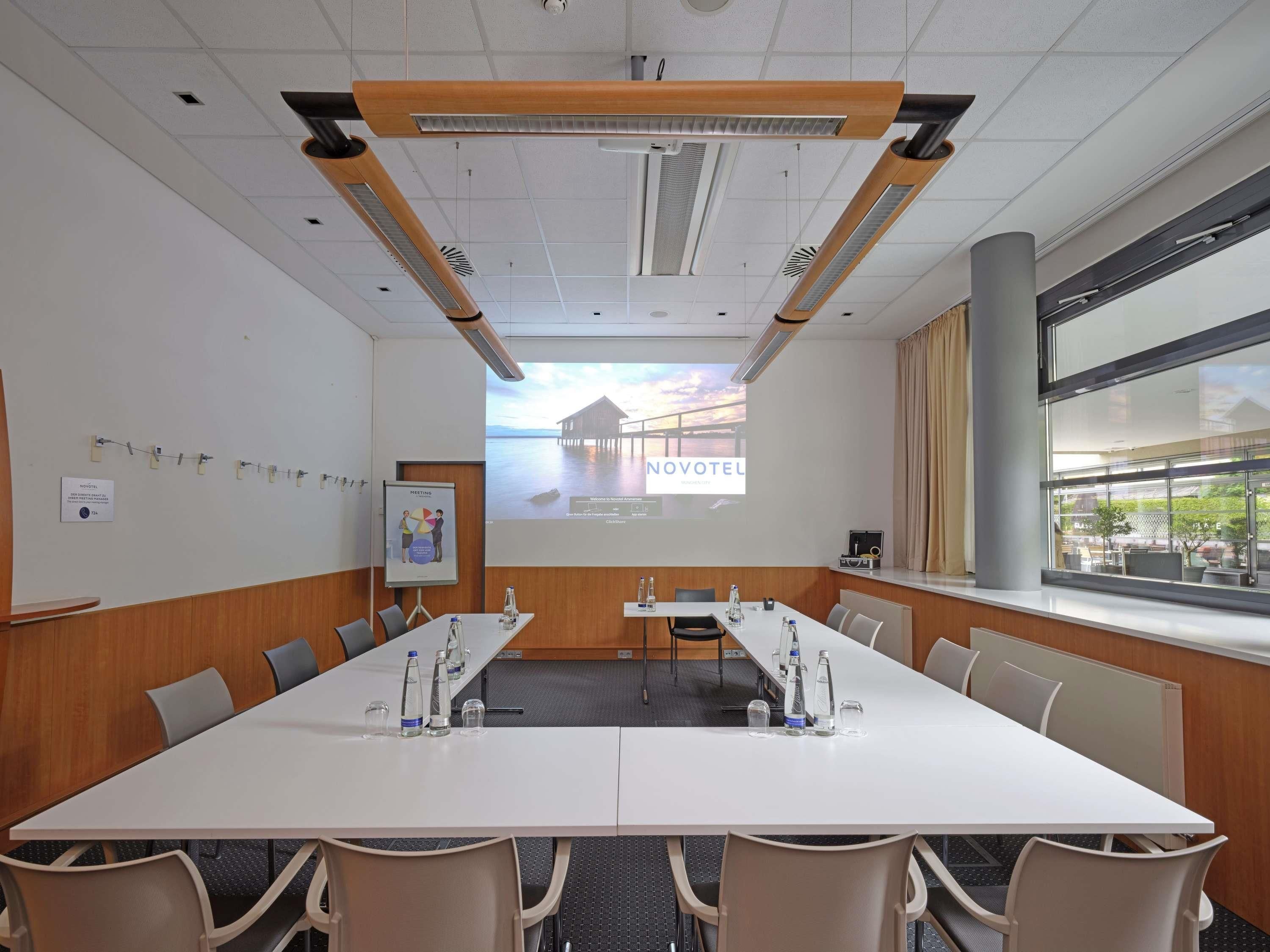 A conference room with a long table, chairs, a projector screen, and a window with a view.