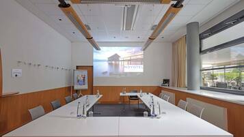 Ein Konferenzraum mit langem Tisch, Stühlen, einer Projektionsleinwand und einem Fenster mit Blick.