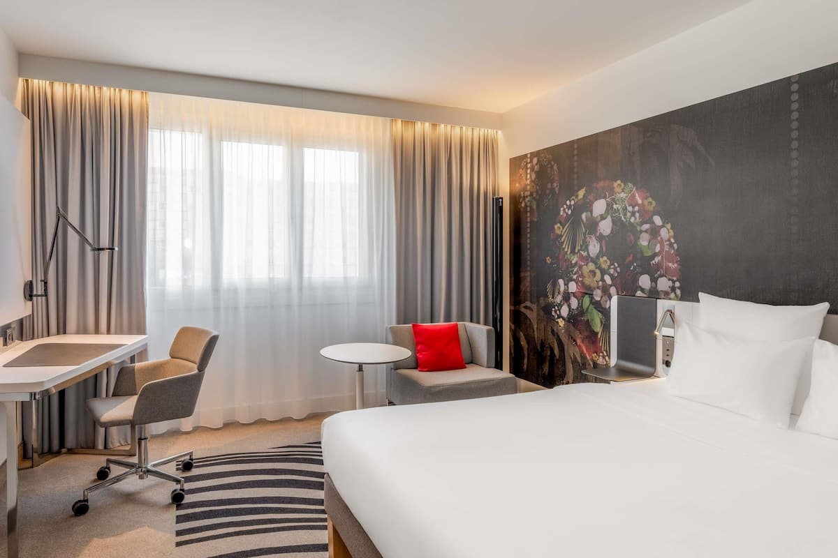 Ein Hotelzimmer mit Bett, Schreibtisch, Stuhl und einem großen Fenster mit Vorhängen.