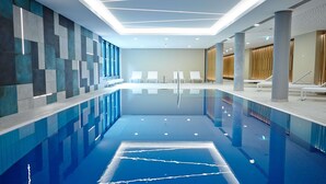 A modern indoor swimming pool with clear water, white lounge chairs, and a geometric wall design. - Novotel Muenchen City (Munich)