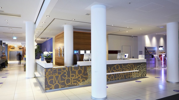 A modern reception area with a reception desk, white pillars, and a patterned wall. - Novotel Muenchen City (Munich)
