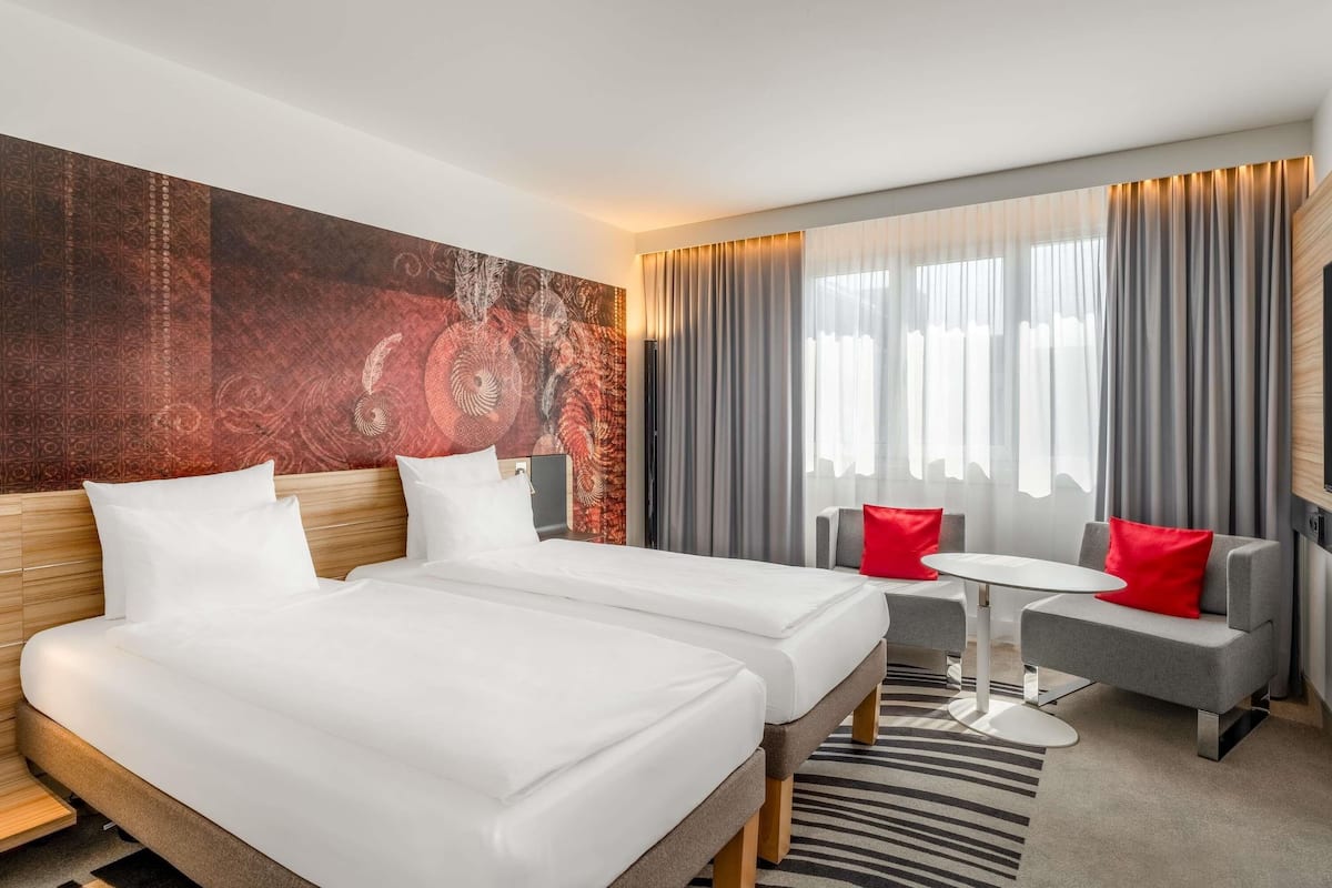 Ein Hotelzimmer mit zwei Betten, einem kleinen Tisch und einer Couch mit roten Kissen.