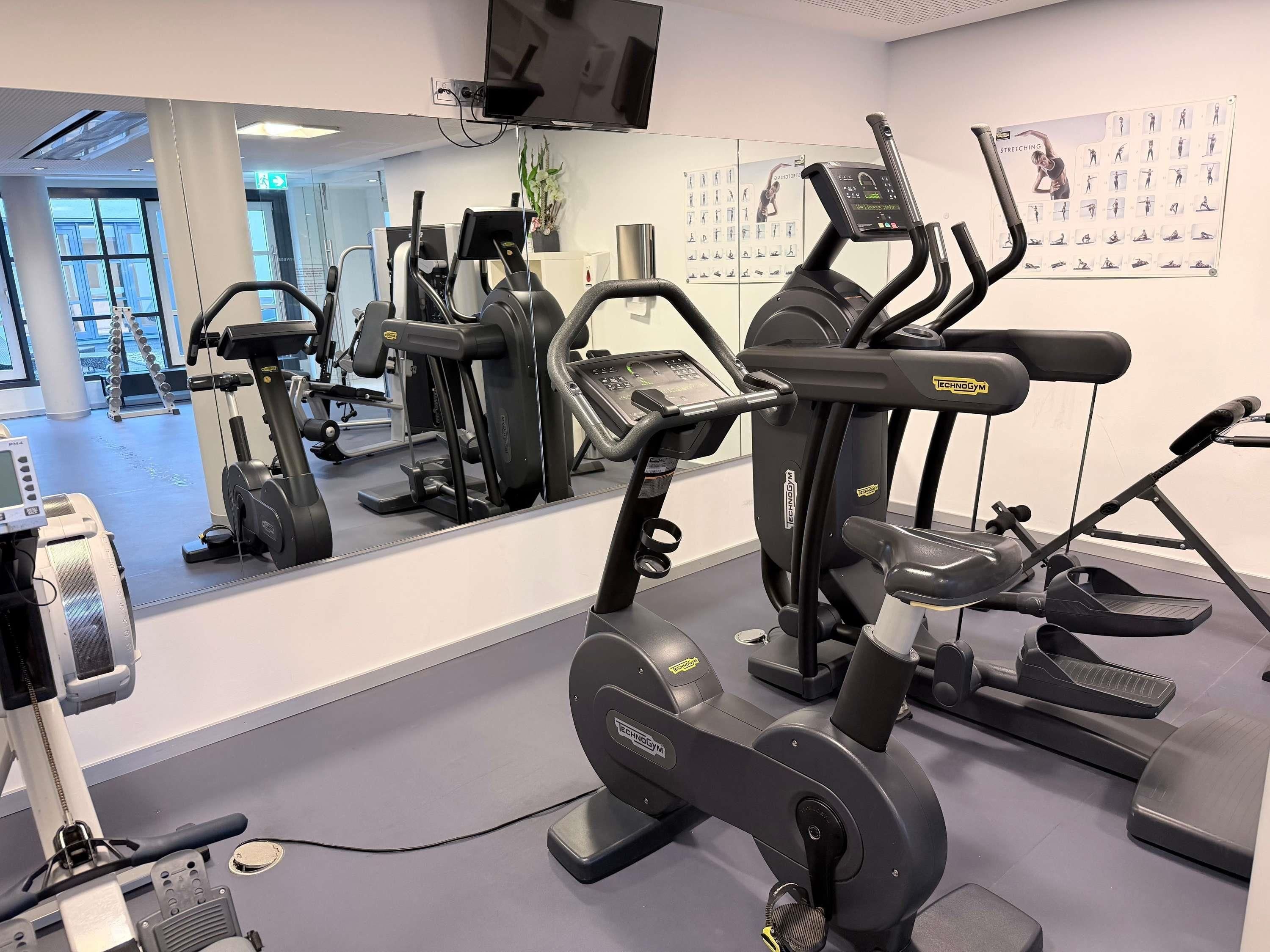A gym with various exercise machines, a large mirror, and a wall with exercise illustrations.